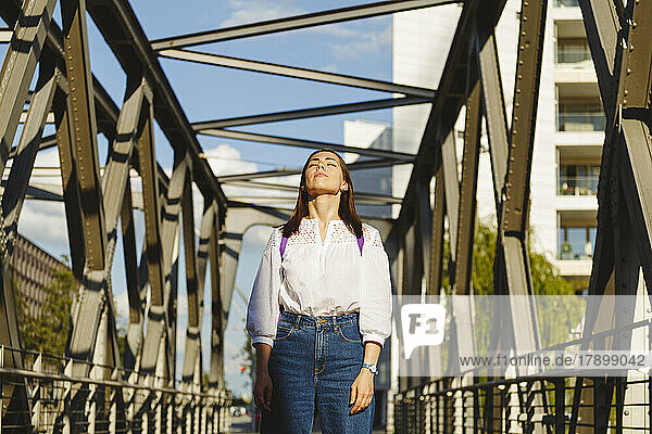 Woman with eyes closed enjoying sunlight on bridge