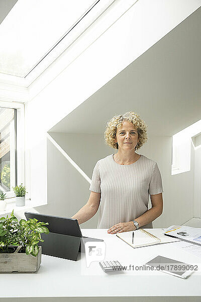 Businesswoman with curly hair standing by desk at home office