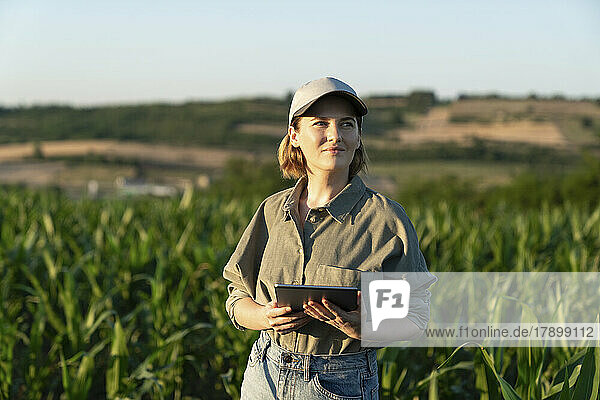 Woman standing with digital tablet in field looking around