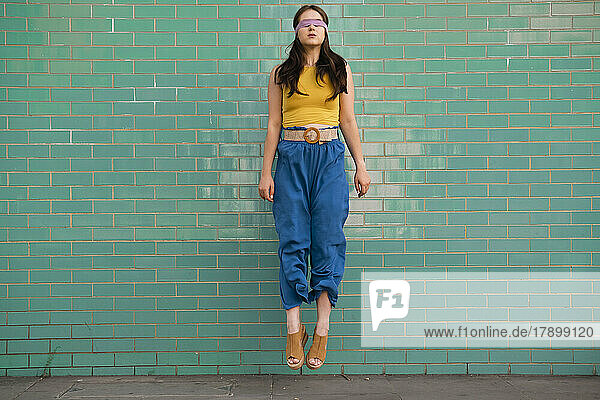Woman with blindfold levitating in front of brick wall