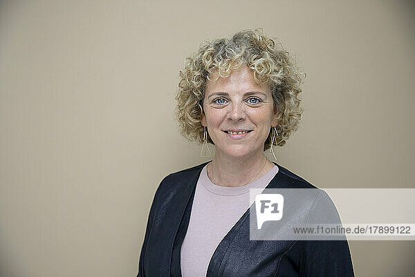 Smiling businesswoman with curly blond hair against brown background