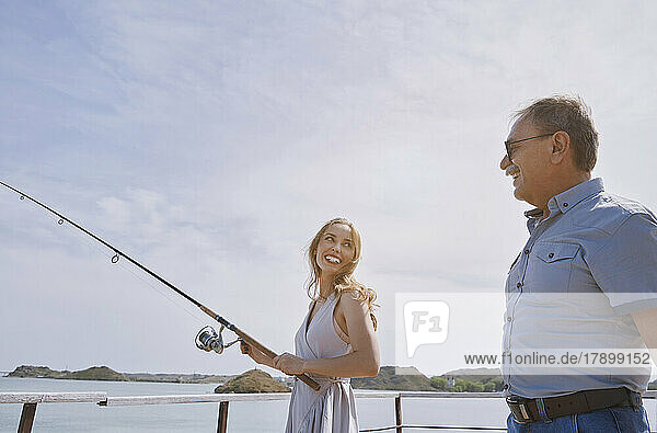 Happy young woman learning fishing from father on weekend