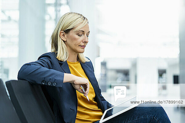 Mature businesswoman using tablet PC sitting on chair in lobby