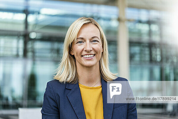 Smiling blond businesswoman in front of building