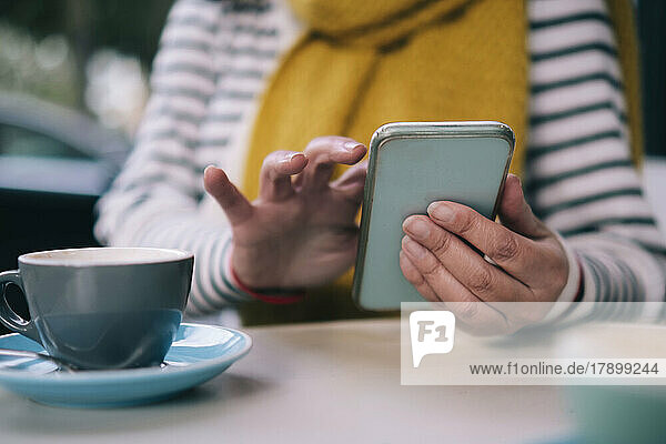 Woman using mobile phone by cup at table in cafe