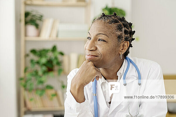 Thoughtful female doctor with hand on chin sitting at home office