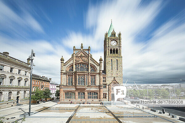 Guildhall with clock tower in city under cloudy sky