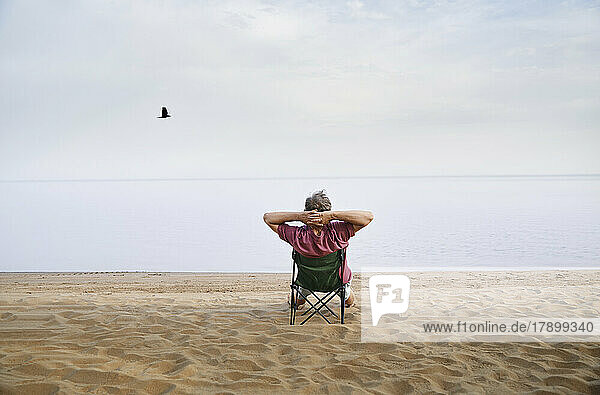 Senior man sitting on folding chair relaxing at beach