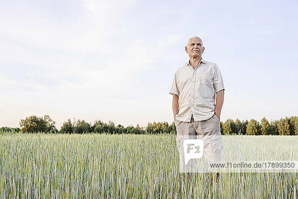 Senior farmer standing with hands in pockets at farm