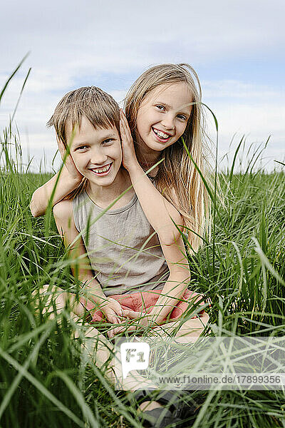 Girl covering ears of brother amidst green grass