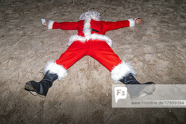 Man wearing Santa Claus costume lying on sand at beach
