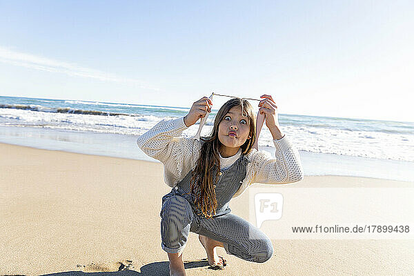 Girl with artificial fish making face at beach