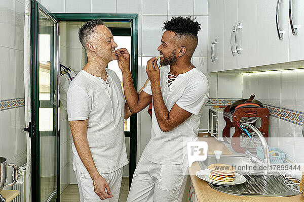 Gay couple eating pancake in kitchen at home