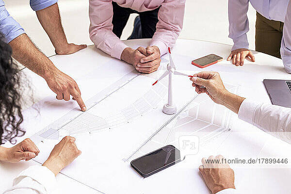 Multiracial business colleagues planning strategy over wind turbine model on table