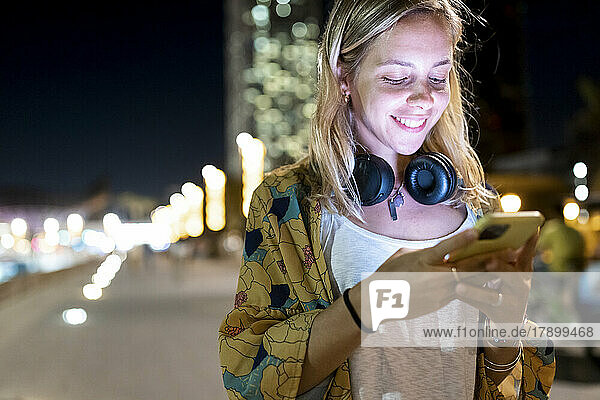 Happy woman with blond hair using smart phone at night