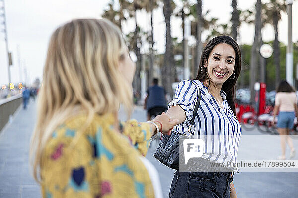 Happy woman holding hands of friend at promenade