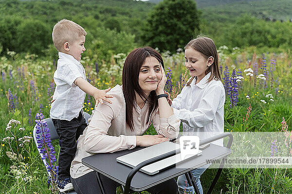 Children playing by mother at desk amidst lupine flowers