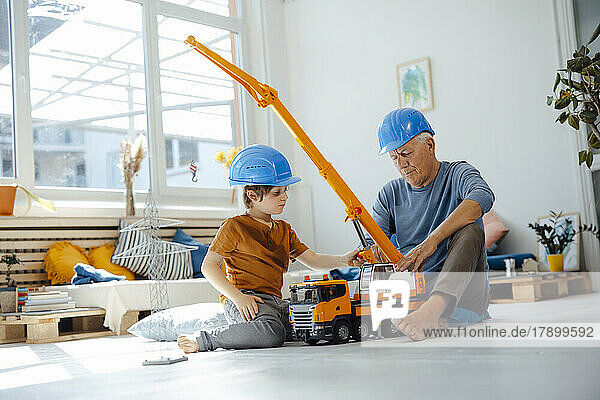 Boy playing with crane toy by grandfather in living room