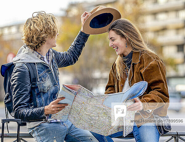 Junger Mann mit Hut und Karte sitzt mit Frau auf Geländer
