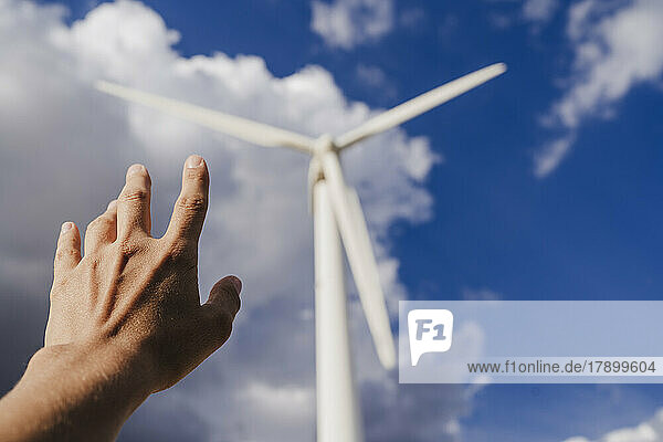 Woman gesturing at tall wind turbine by sky