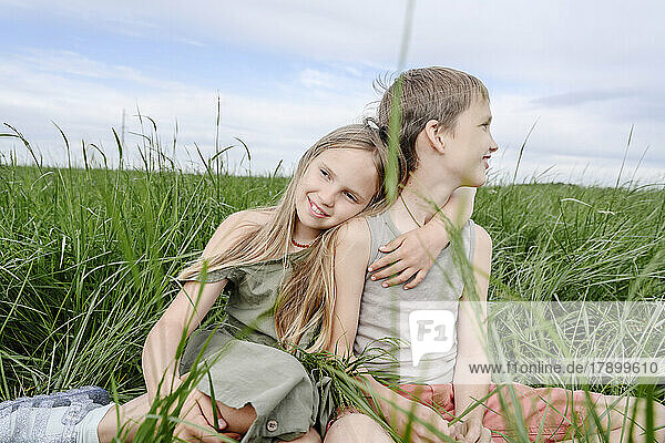 Brother and sister sitting together at grassy field