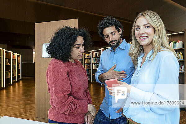 Smiling woman sharing smart phone with colleagues in library