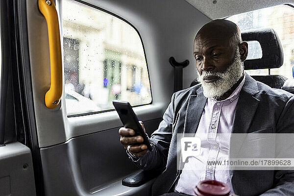 Senior passenger using mobile phone in back seat of taxi