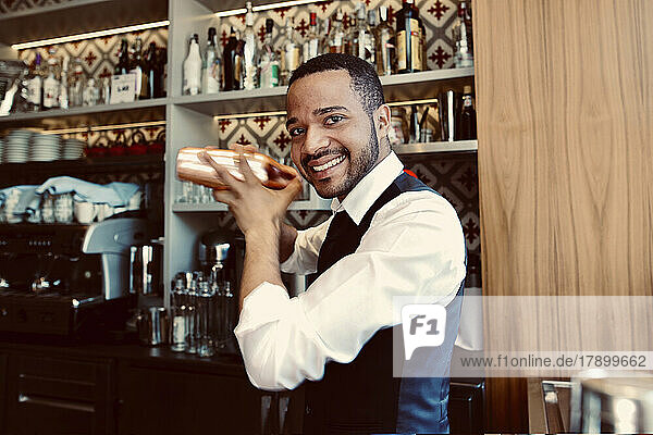 Smiling bartender shaking cocktail shaker at bar