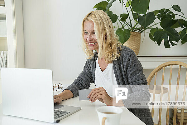 Smiling woman holding credit card using laptop at home