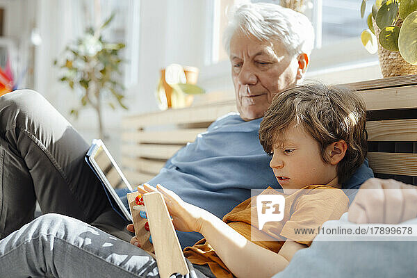 Grandfather looking at grandson with abacus sitting on sofa