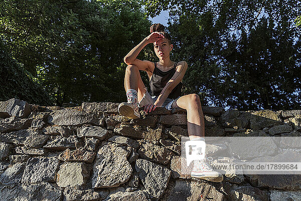 Nicht-binärer Hipster sitzt auf einer Steinmauer