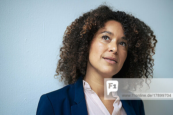 Thoughtful businesswoman with curly hair in front of wall