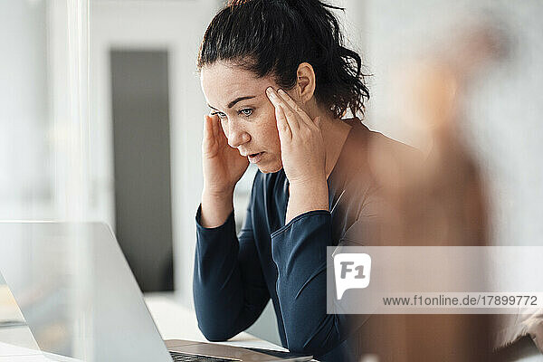 Stressed businesswoman with head in hands looking at laptop on table