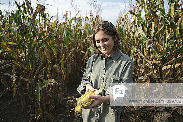 Smiling woman holding corncob in field