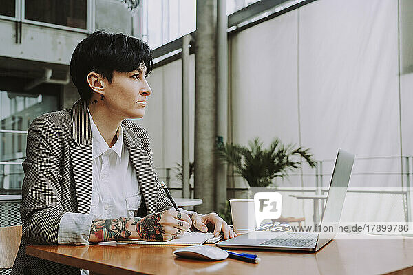 Geschäftsfrau sitzt mit Laptop und Notizblock im Café