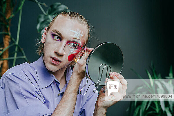 Man applying make-up on face looking in hand mirror