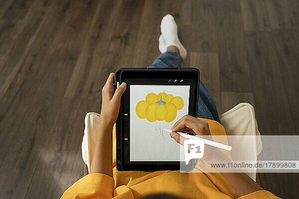 Mädchen zeichnet zu Hause mit digitalisiertem Stift gelben Kürbis auf Tablet-PC