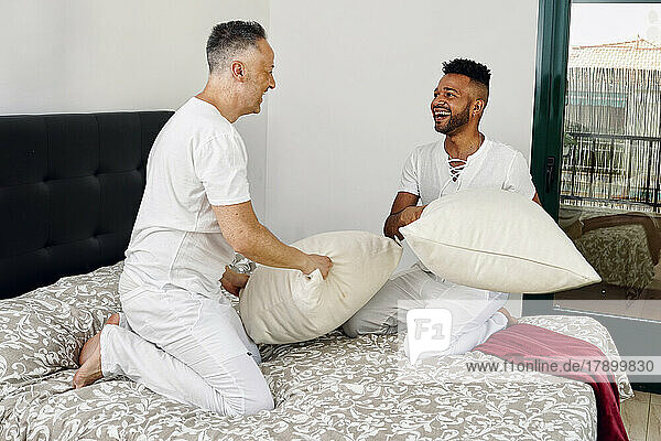 Playful gay couple pillow fighting in bedroom at home