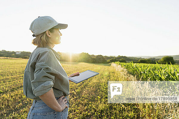 Frau steht mit digitalem Tablet im Feld und schaut sich um
