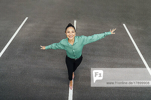 Happy businesswoman with arms outstretched balancing on road marking