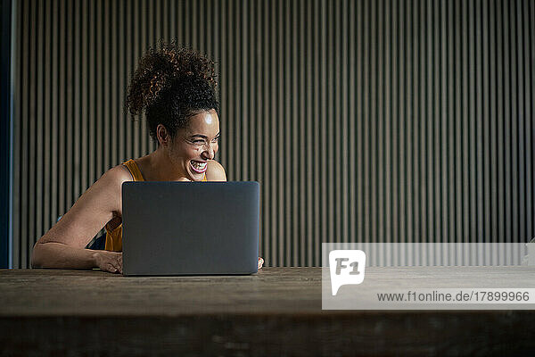 Happy businesswoman with laptop on table in front of wall