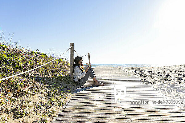 Girl reading book leaning on pole at beach