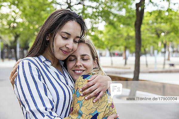Smiling young women with eyes closed hugging each other at park