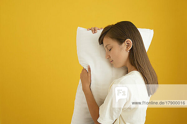 Girl with eyes closed resting her face on pillow against yellow background