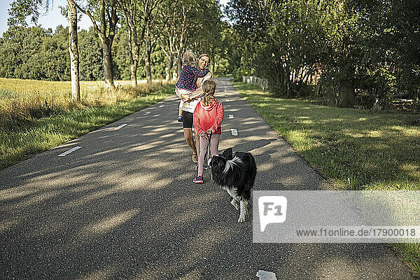 Mother walking with daughters and dog on road
