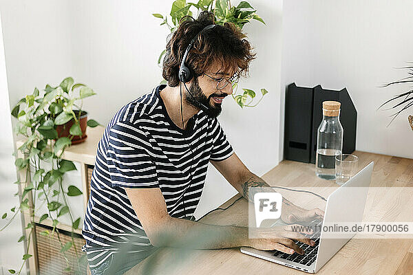 Smiling freelancer using laptop wearing headset in home office