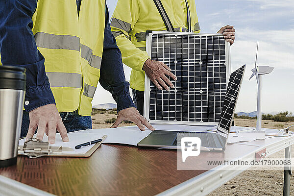 Ingenieure arbeiten mit Laptop und Solarpanel am Schreibtisch im Windpark zusammen