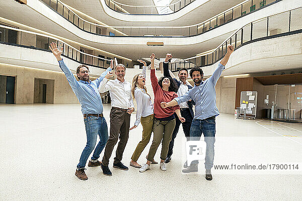 Happy business colleagues with arms raised standing in lobby