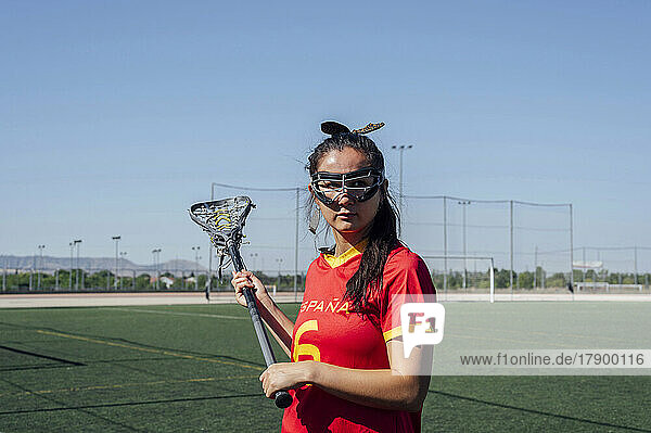 Young woman with lacrosse stick standing on field