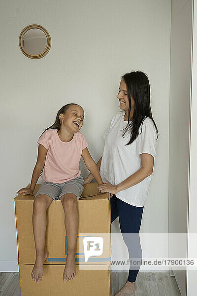 Mutter blickt glückliche Tochter an  die auf einer Kiste sitzt